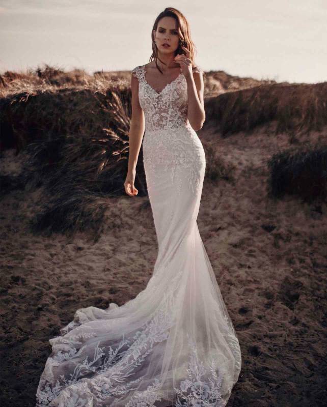 Woman modelling white lace fitted wedding dress with train on a beach