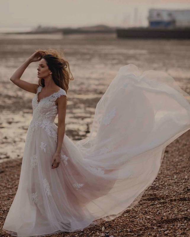 Woman modelling white lace wedding dress on a windy beach