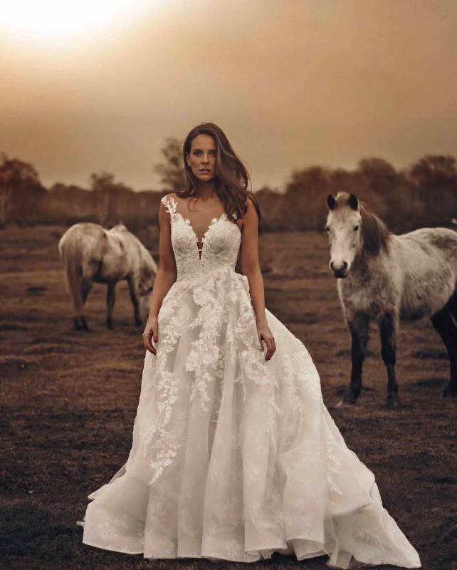 Woman modelling white lace wedding dress with ponies in background